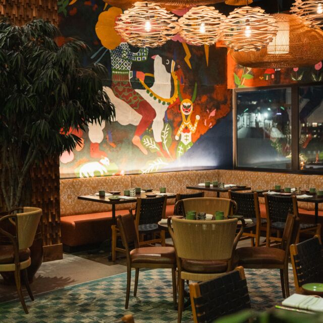 A dining area with tables and chairs, a mural on the wall, and unique lighting.