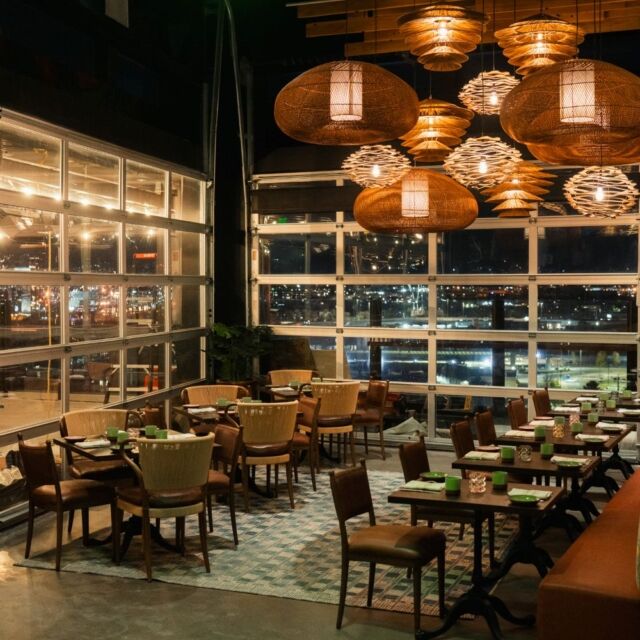 A dining area with large windows, wicker light fixtures, and multiple dining tables set with green cups and plates.
