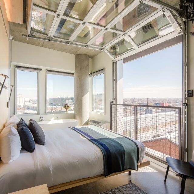 A wide view of a hotel room with a bed, window, and balcony